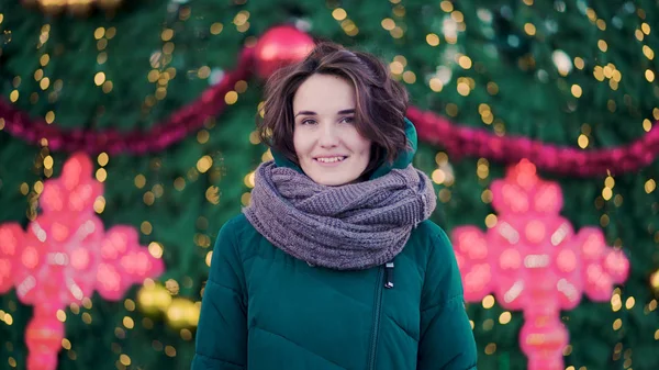 Bella giovane donna carina con una sciarpa sulla strada sullo sfondo dell'albero di Natale. Stile urbano — Foto Stock