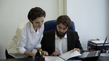 Genç bir kadın işçi patron belgeleri gösterir. İşçisi kadın rapor şefe gösterir.