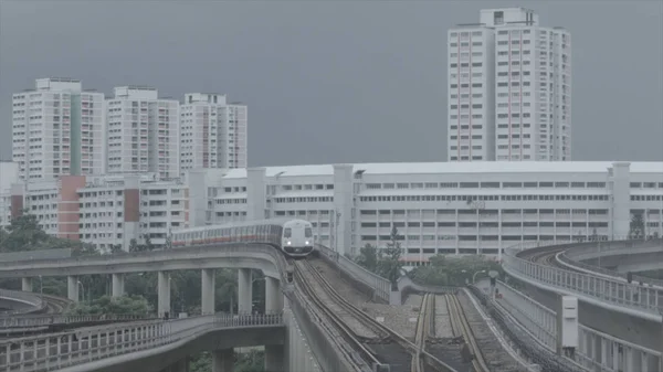 Tren de metro moderno en un ferrocarril en Sinapore en un fondo de edificios de la ciudad. Le dispararon. Singapur tren rápido de masas MRT viaja por la vía . —  Fotos de Stock