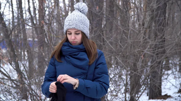 Hermosa chica de pie en el bosque de invierno y con guantes, fondo de ramas nevadas. Bosque de invierno paisaje fondo. Una joven con ropa de invierno, camina por el bosque — Foto de Stock