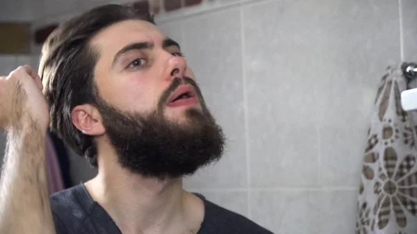 Man in the bathroom looking in a mirror and fixing his hair. Portrait of handsome man brushing his hair in bathroom. Reflection in the mirror of handsome man styling hair — Stock Photo, Image