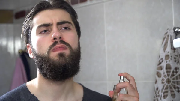 Handsome man using perfume in front of mirror. Handsome man applying perfume at the morning