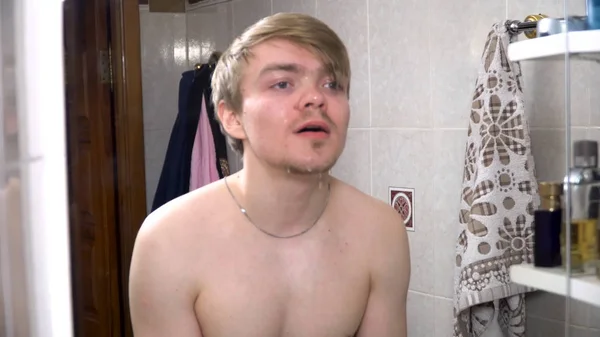 Joven rociando agua en su cara después de afeitarse, salpicando agua en su cara. Hombre lavándose la cara con agua limpia delante de un espejo en el baño. El chico lavándose la cara por la mañana —  Fotos de Stock