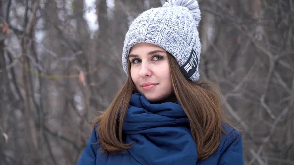 Ładna kobieta w zimowych kapelusz uśmiech stojący na zewnątrz na śniegu, w lesie, z tle zaśnieżonych schody. Portret dziewczyny piękne patrząc w kamerę. Zimowe Portret młodej dziewczyny. The Zdjęcie Stockowe