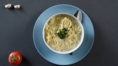 Bir tabak erişte ile tavuk çorbası. Sahne. Tavuk çorbası krem renkli seramik kase kulplu. Tabak kraker ve çorba kasesi arka planda.