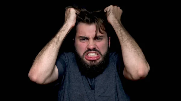 Wütender junger Mann schreit, drückt negative Emotionen aus, reißt sich die Haare aus, isoliert auf schwarzem Hintergrund. Nahaufnahme eines gestressten jungen Mannes, der schreit und schreit — Stockfoto