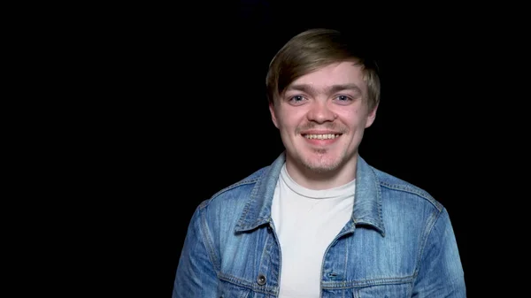 Modelo bonito jovem sobre fundo preto em uma jaqueta de jeans dá um sorriso alegre. Jovem barbudo homem dá um grande sorriso . — Fotografia de Stock