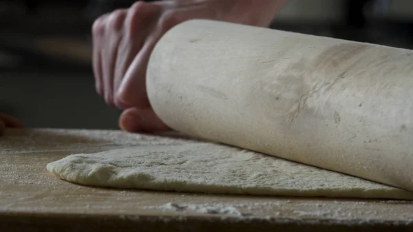 Hombre extendiendo la masa en la mesa de la cocina, de cerca. Escena. El cocinero enrolla un trozo de masa en la mesa de la cocina con un rodillo. Vista de cerca. Concepto de cocina y comida casera —  Fotos de Stock