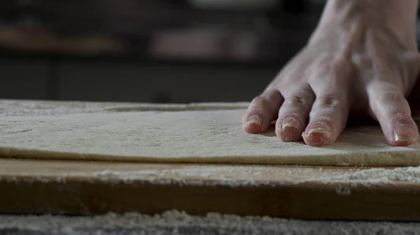 Hombre extendiendo la masa en la mesa de la cocina, de cerca. Escena. El cocinero enrolla un trozo de masa en la mesa de la cocina con un rodillo. Vista de cerca. Concepto de cocina y comida casera — Foto de Stock