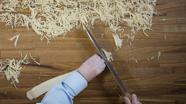 Manos de vista superior del chef haciendo fideos caseros de huevo. Escena. Las manos de Baker cortando la masa. Vista superior de las manos masculinas con el cuchillo cortando masa - haciendo pasta o fideos — Foto de Stock