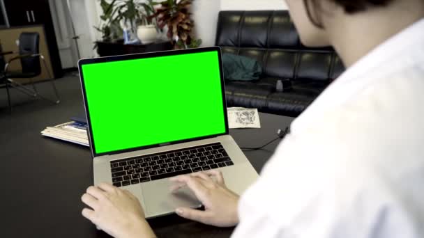 Over the shoulder shot of a woman using computer laptop with green screen display in office. Business woman using laptop with blank green screen on wooden table in office — Stock Video