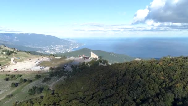 Panorama van de bergen bedekt met groene bos, met een moderne Europese stad aan de oever van de zee op een schone wolkenloze dag. Schot. Luchtfoto uitzicht op de stad door de oever — Stockvideo