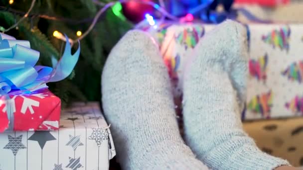 Bílé pletené ponožky na ženské nohy pozadí nazdobený vánoční stromeček. Svátků a nového roku koncept. Vyšívané pletené ponožky s vánoční strom v pozadí