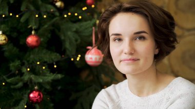 Noel kavramı, yaratıcı bir şekilde dekore edilmiş bir Noel ağacı arka plan üzerinde gülümseyen güzel esmer. Noel ağacın arkasında kamerayla gülümseyen güzel genç kadın portresi kapatın