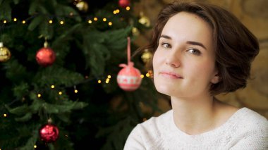 Noel kavramı, yaratıcı bir şekilde dekore edilmiş bir Noel ağacı arka plan üzerinde gülümseyen güzel esmer. Noel ağacın arkasında kamerayla gülümseyen güzel genç kadın portresi kapatın