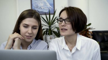 Birlikte çalışan, modern ofis dizüstü bilgisayar ekranı önünde fikirleri tartışmak iki genç, güzel benzetmeler. İki meslektaşları bir masada oturan iş için dizüstü bilgisayar kullanarak.