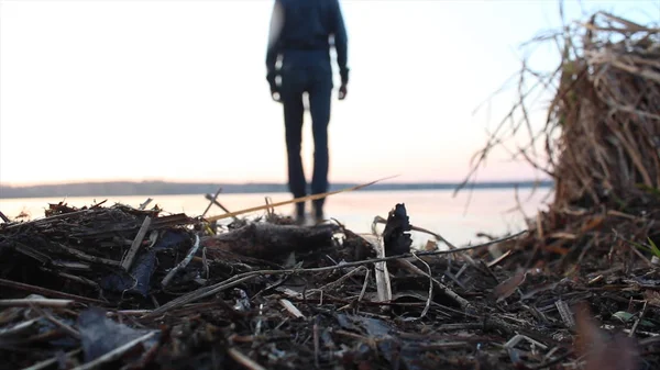 Visão traseira de um homem que vai para o lago no outono no fundo do céu borrão do sol. Close up para withered, amarelo, grama molhada e um homem atrás indo para a água fria do lago . — Fotografia de Stock