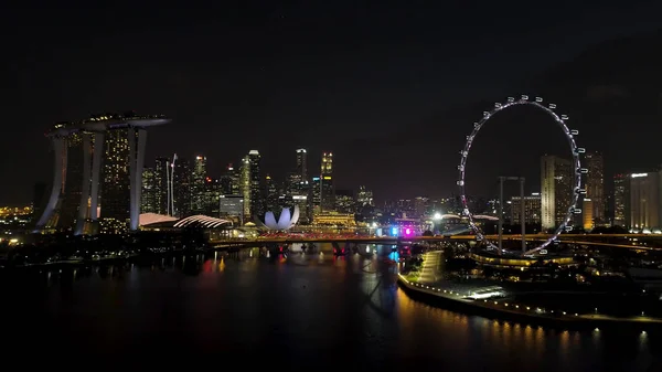 Singapore - 25 September 2018: luchtfoto van grote stad met veel licht bewolkte hemel en reuzenrad 's nachts. Schot. Mooie grote stad achter het meer met uitzicht op een reuzenrad en veel 's nachts — Stockfoto