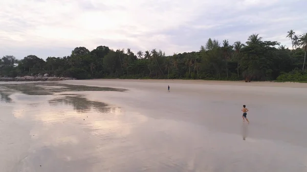 Aerial for man jogging on a tropical sandy beach near the sea. Shot. Beautiful aerial view of a runner man training on the beach. — Stock Photo, Image