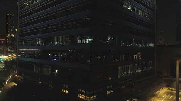 Singapour - 25 septembre 2018 : Vue frontale de la façade nocturne du bâtiment avec beaucoup de fenêtres éclairées. Fusillade. Façade du bâtiment multi-étages de verre et d'acier, bureaux et travailleurs à l'intérieur — Photo