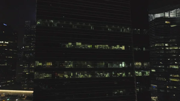 Vue frontale de la façade nocturne du bâtiment avec beaucoup de fenêtres éclairées. Fusillade. Façade du bâtiment multi-étages de verre et d'acier, bureaux et travailleurs à l'intérieur, fond de la vie nocturne de la ville — Photo