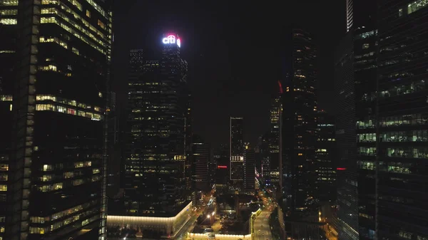 Singapur - 25 de septiembre de 2018: Vista frontal de la fachada nocturna del edificio con muchas ventanas iluminadas. Le dispararon. Fachada el edificio de varios pisos de vidrio y acero, oficinas y trabajadores en el interior —  Fotos de Stock
