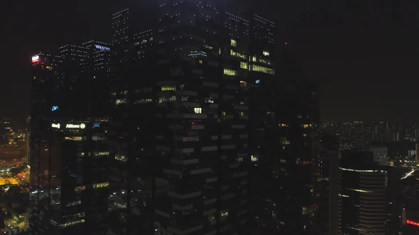 Singapore - 25 September 2018: Windows met mensen die werkzaam zijn in het interieur van een kantoorgebouw in de nacht in de grote stad. Schot. Grote stad nachtleven, sluiten voor mooie glazen gevel wolkenkrabber — Stockfoto