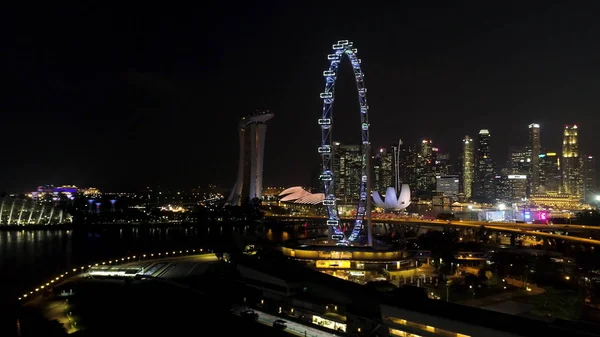 Singapore - 25 September 2018: Singapore city skyline på natten med floden, lila upplysta pariserhjulet och berömda Marina Bay Sands Hotel. Skott. Hisnande Flygfoto över natt Singapore med — Stockfoto
