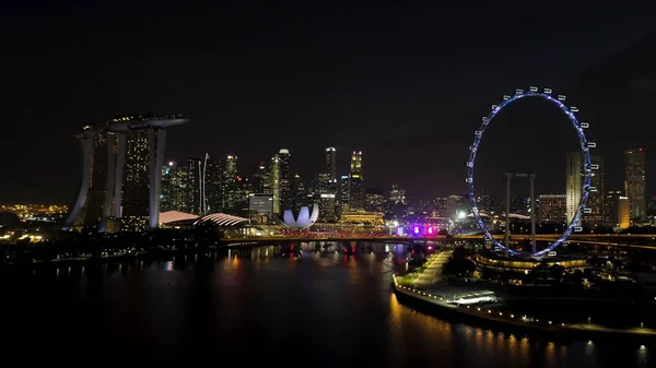 Singapore - 25 September 2018: Singapore city skyline på natten med floden, lila upplysta pariserhjulet och berömda Marina Bay Sands Hotel. Skott. Hisnande Flygfoto över natt Singapore med — Stockfoto