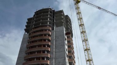 Alt görünümü yüksek bina sarı vinç yakınındaki bitmemiş inşaat mavi, bulutlu gökyüzü arka plan üzerinde. Bir yaz, güneşli günde metal vinç yakınındaki yapım aşamasında bina yüksek doğmak.