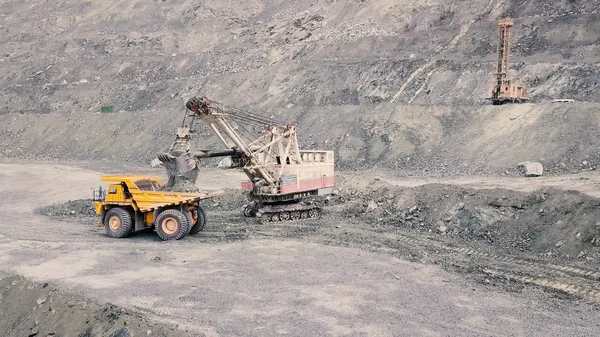 Excavadora y camión volquete mientras carga mineral de piedra en una cantera gris, industria minera. Acciones. La excavadora pesada carga mineral de roca en un camión minero grande de cuerpo volcado, equipo de cantera . — Foto de Stock