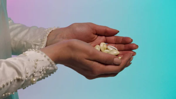 Close up for eastern young woman hands giving many small seashells to man hands, barter concept. Stock. Eastern woman in white dress holding and passing many small seashels to a man.