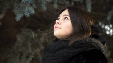 Genç, çekici kız bir kürk manto ve örme eşarp bir kış park, sokak moda arıyorsunuz için kapatın. Kış giysileri çam dalları arka plan üzerinde güzel kadın portresi.