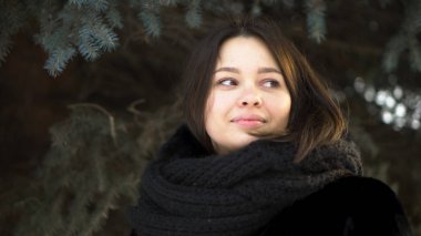 Genç, çekici kız bir kürk manto ve örme eşarp soldaki bir kış Park, sokak moda arıyorsunuz için kapatın. Kış giysileri çam dalları arka plan üzerinde güzel kadın portresi.