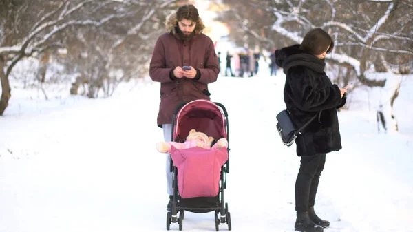 Madre y padre adictos a los teléfonos móviles descuidando al bebé en el cochecito y mientras caminan en el parque de invierno. Los padres ocupados con los teléfonos inteligentes ignorando a los niños pequeños en el cochecito, la adicción, el concepto de valores . —  Fotos de Stock