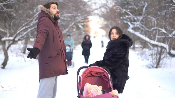 Los padres jóvenes se gritan unos a otros cerca de un bebé en un cochecito rosa mientras caminan en el parque de invierno. Madre y padre enojados discutiendo al aire libre, descuidando a su hijo, problemas familiares jóvenes . —  Fotos de Stock