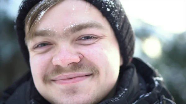 Porträtt av stilig, gladlynt man med mustasch iklädd vinterkläder med snö på hans ansikte. Närbild för blond man med blå ögon som ler i en solig, vinterdag. — Stockfoto