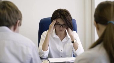 Women boss in stress of job employees. Businesswoman tired of mistakes in work of employees. Attractive boss suffers from headache and fatigue, removes glasses in office