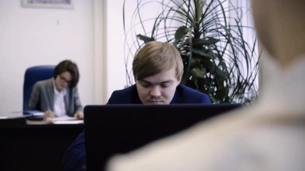 Young man throws crumpled papers. Young worker communicates and is naughty, throwing paper ball at colleague during working hours at table in office — Stock Video