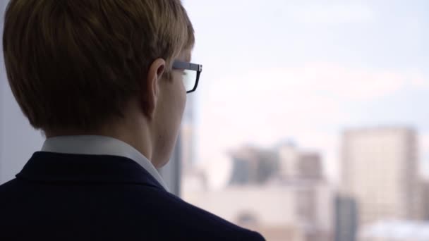 Un hombre de negocios de cerca mirando por la ventana. Joven gerente con expresión reflexiva mira por la ventana a través de gafas y piensa en el trabajo — Vídeos de Stock