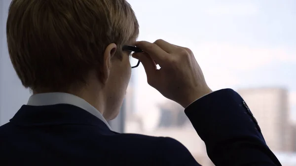 Un hombre de negocios de cerca mirando por la ventana. Joven gerente con expresión reflexiva mira por la ventana a través de gafas y piensa en el trabajo — Foto de Stock