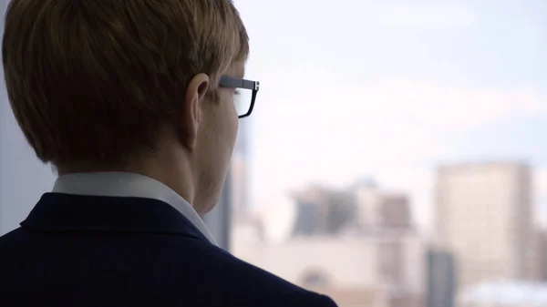 Un hombre de negocios de cerca mirando por la ventana. Joven gerente con expresión reflexiva mira por la ventana a través de gafas y piensa en el trabajo — Foto de Stock