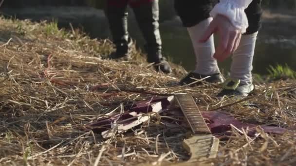 Homme en vieux costume et perruque blanche ramassant partie de guitare cassée de l'herbe sèche, concept de spectacle historique. Des actions. Hommes en vêtements anciens de 17 siècle prenant cou de guitare sur fond de forêt verte . — Video