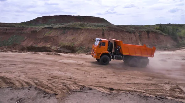 View of driving dump truck on sandy soil. Scene. Orange dump truck rides on quarry with ground in lowlands