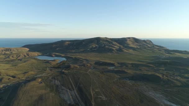 Πανοραμική Αεροφωτογραφία του πεδίο καταπράσινη, ψηλά βουνά κοντά σε μικρή λίμνη μπλε της θάλασσας και συννεφιασμένο ουρανό φόντο. Βολή. Όμορφο τοπίο με υψηλού καταπράσινους λόφους και την κοιλάδα κοντά στη θάλασσα. — Αρχείο Βίντεο