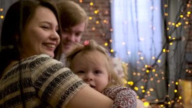 Kız bebek gülümseyen mutlu anne Noel için sarı çelenk oda dekore edilmiştir. Baba, anne ve küçük çocuk birlikte yeni yıl kutlama.