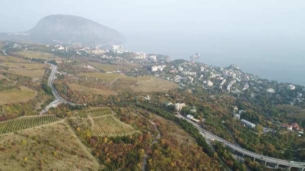Aerial landscape view of a beautiful bay with forest and hills, small town, and motorway. Shot. Beautiful foggy scenery of autumn yellow fields, highway, and coastal city near the sea. — Stock Video