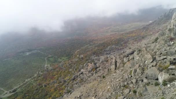 Paisagem natural, vista do topo da colina no vale amarelo e verde em névoa espessa. Atingido. Aéreo para inclinação íngreme de uma montanha, campos verdes e secos em nuvens nebulosas . — Vídeo de Stock