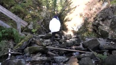 Küçük, güzel şelale yakınındaki dağlarda seyahat şapka ve Beyaz ceketli adamı görünümünü arka. Görüntüleri. Komuta sizde yürüyüş çarpıcı şelale, macera, seyahat, turizm kavramı.