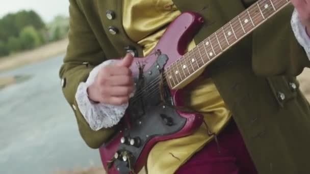 Gros plan pour homme avec une guitare électrique violette jouant dans un costume à l'ancienne de manière rococo sur fond d'herbe flétrie. Des actions. Artiste en vêtements anciens joue de la guitare avec varech suspendu . — Video